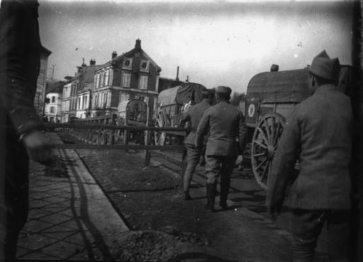 Convois de charriots (vue 1) et de soldats en voiture à cheval traversant un village (vue 2).